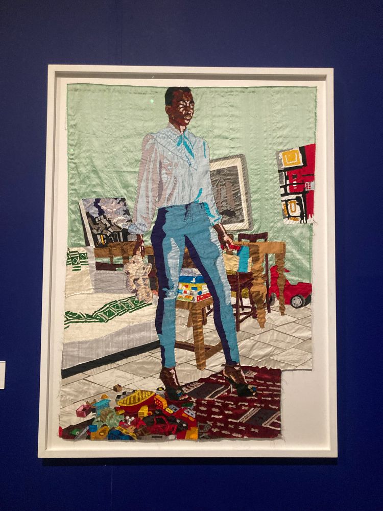 A silk tapestry of a black woman artist artist standing triumphantly in a living space by Billie Zangewa
