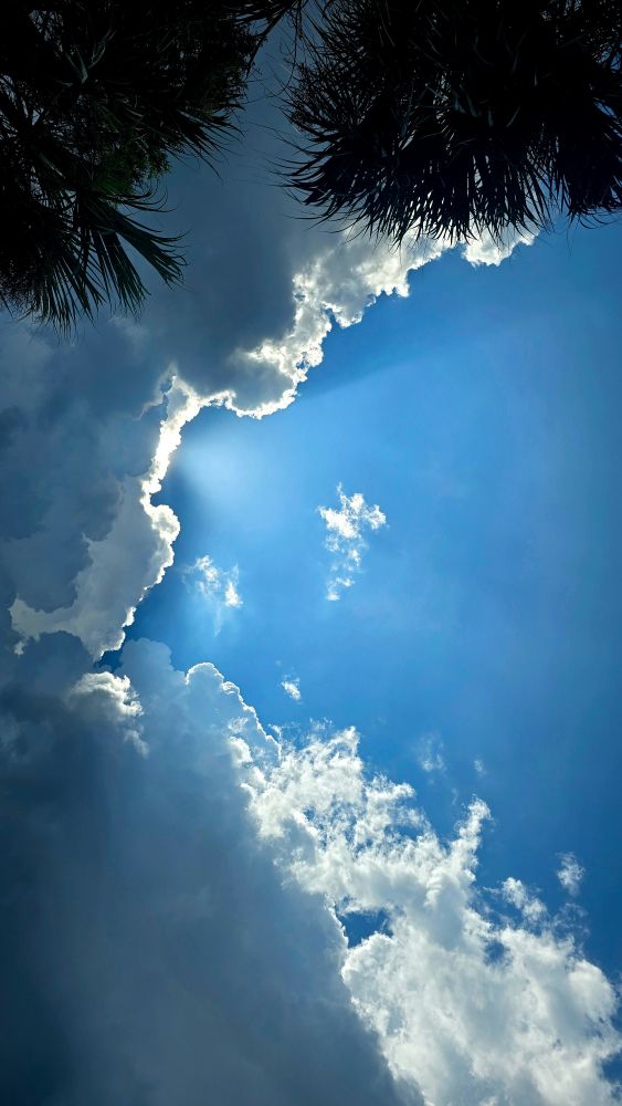 Sunlight beaming out into blue sky from behind heavy cloud cover.