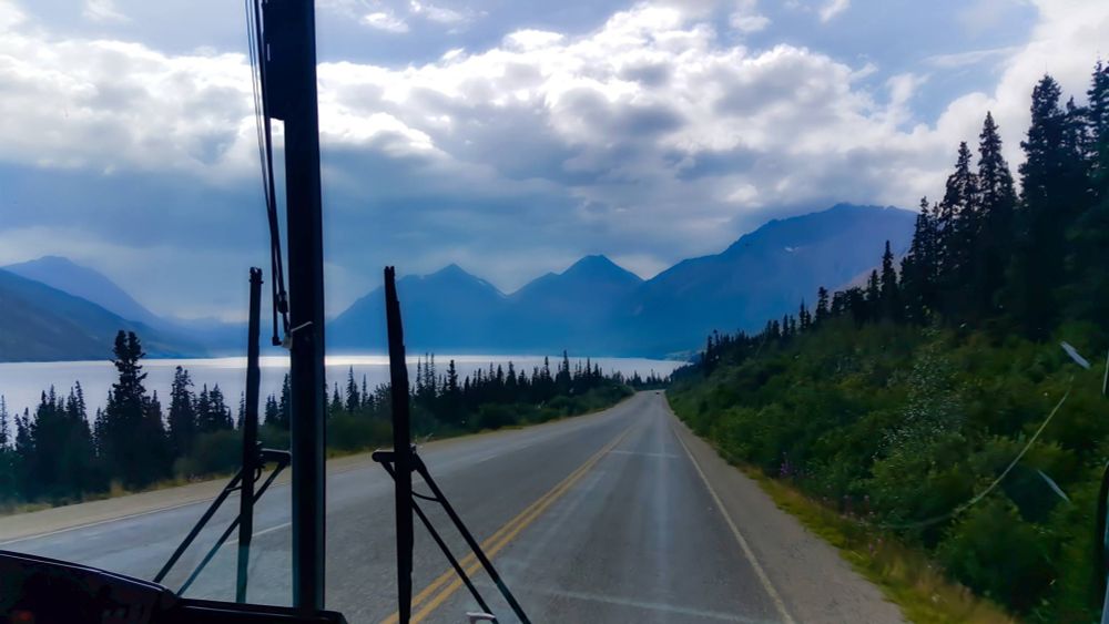 Dramatic scene from the confines of a truck cab: two-lane highway, lake with lighting, and steep mountains.