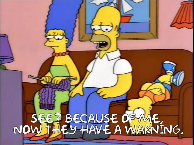 Marge and Homer are sitting on their sofa, Marge is knitting, and Bart is lying upside down on the other side. Homer references the ad that just played on the television, saying, "See? Because of me, now they have a warning."