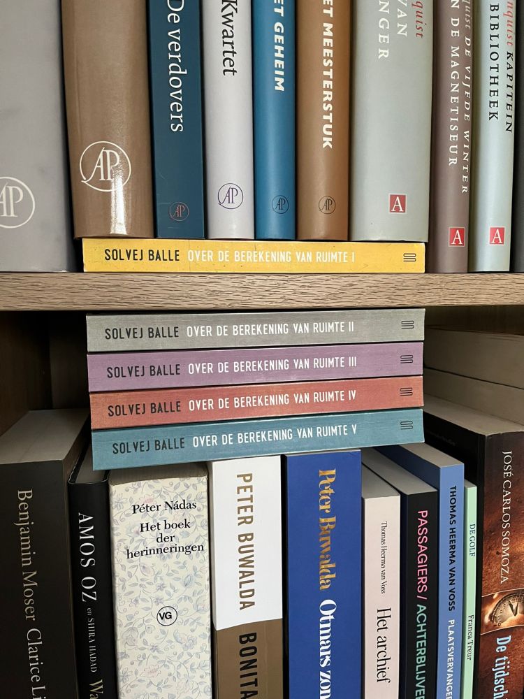 Vijf delen van het boek "Over de berekening van ruimte" door Solvej Balle, in een boekenkast, maar dan wel op elkaar gestapeld net onder én boven een plank zodat het nogal opvalt maar totaal niet past bij de indeling van de rest