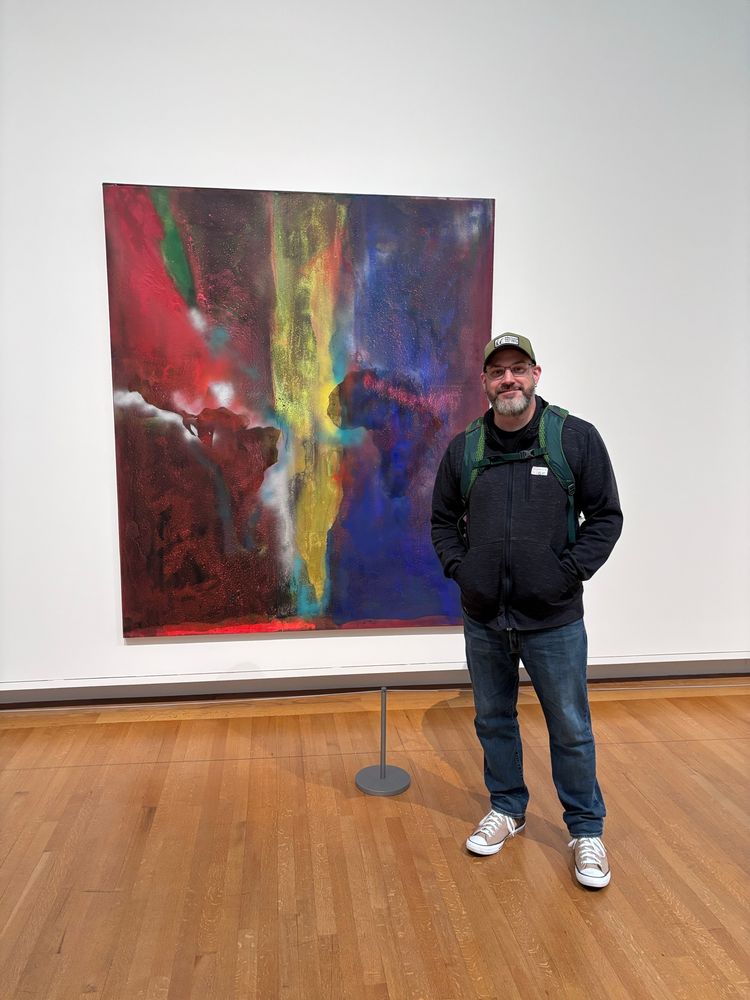 A philosopher standing in front of a painting by Frank Bowling titled Night Journey.