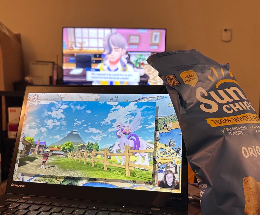 a picture in my living room, from my perspective, featuring a laptop playing a pokemon-related youtube video, a bag of sun chips, and my TV where I'm playing pokemon violet
