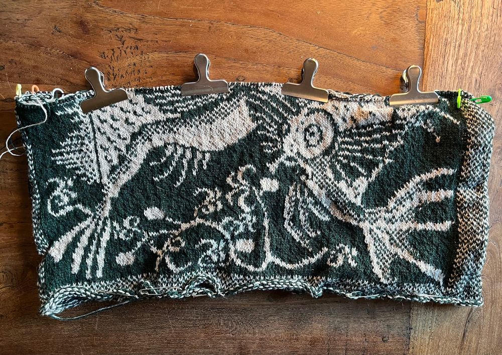 Half-finished knitted cushion cover with fish motif. Colours are dark green and white.