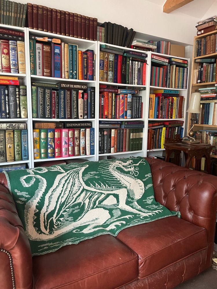 Large green knitted blanket with a dragon motif on a leather sofa against a bookcase.