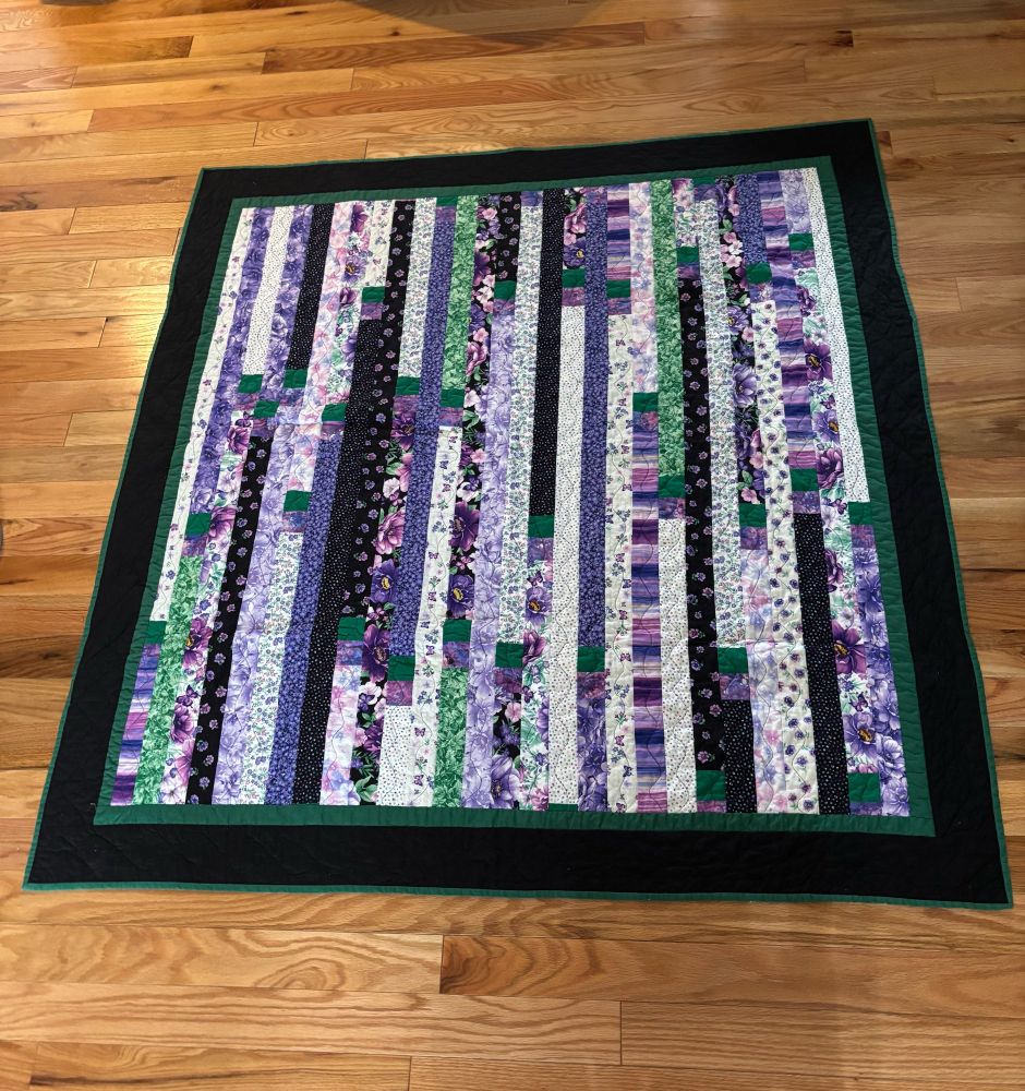 Photo is of a quilted throw made of jelly roll strips with two borders-green and black.