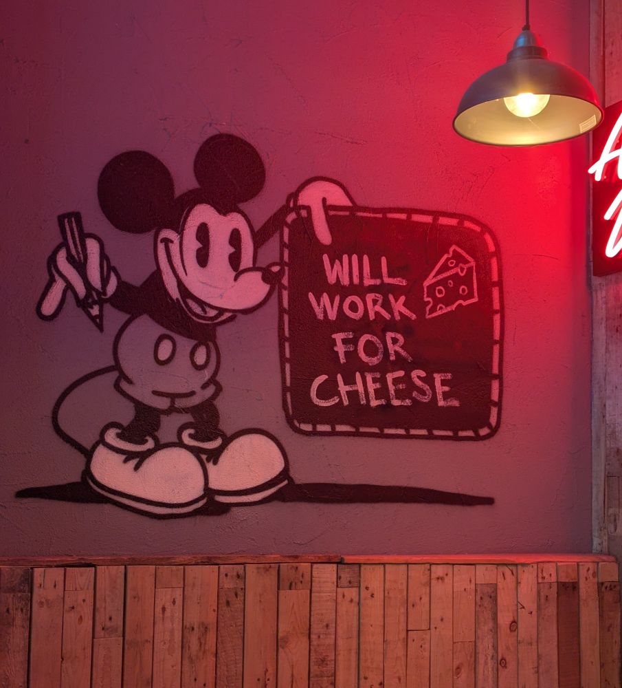 A snapshot of a painting of Mickey Mouse holding a sign that says "Will work for cheese."
