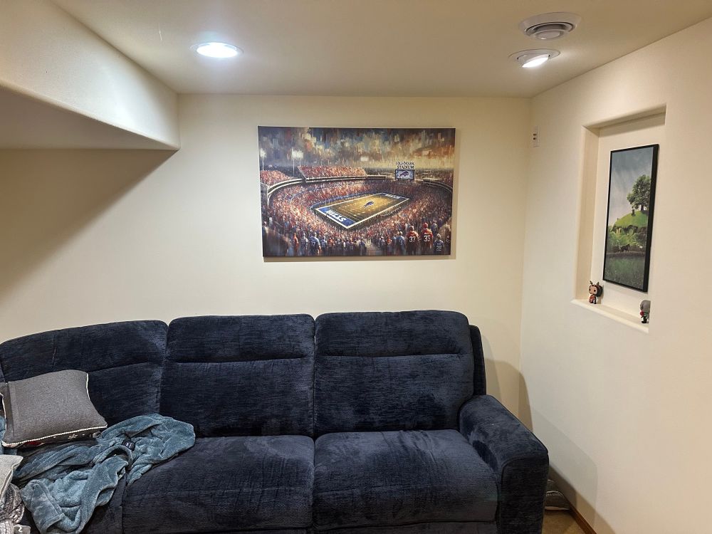 A canvas print of Highmark Stadium hung above a blue couch in a cool basement.