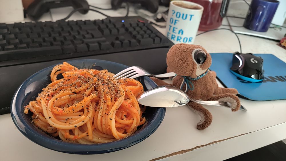 A plush octopus next to a bowl of pasta (Spaghettoni with vegan Pesto Calabrese and ground black pepper)