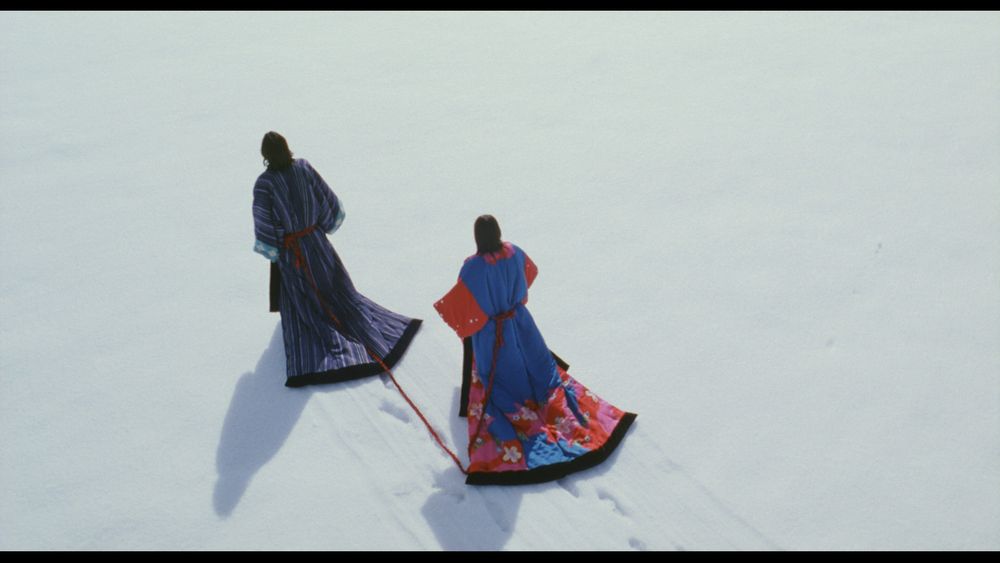 a screenshot from the movie dolls of a couple walking through snow. they're bound together by rope