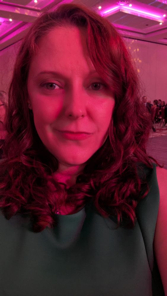 Selfie of me in a green dress in a room with soft pink lighting.