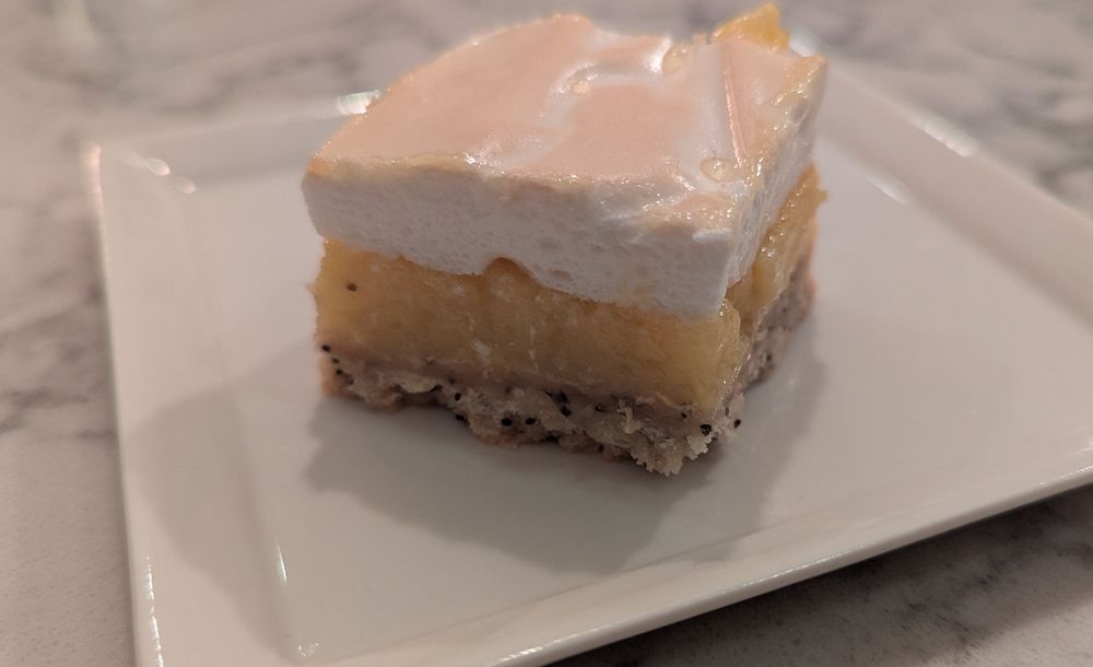 A very nice looking lemon meringue bar on a small, square ceramic plate