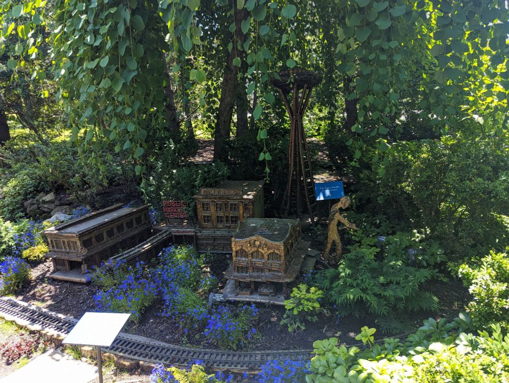 Miniature Seattle, complete with Space Needle, set along outdoor model railroad tracks that run under lush green trees at the Chicago Botanic Garden