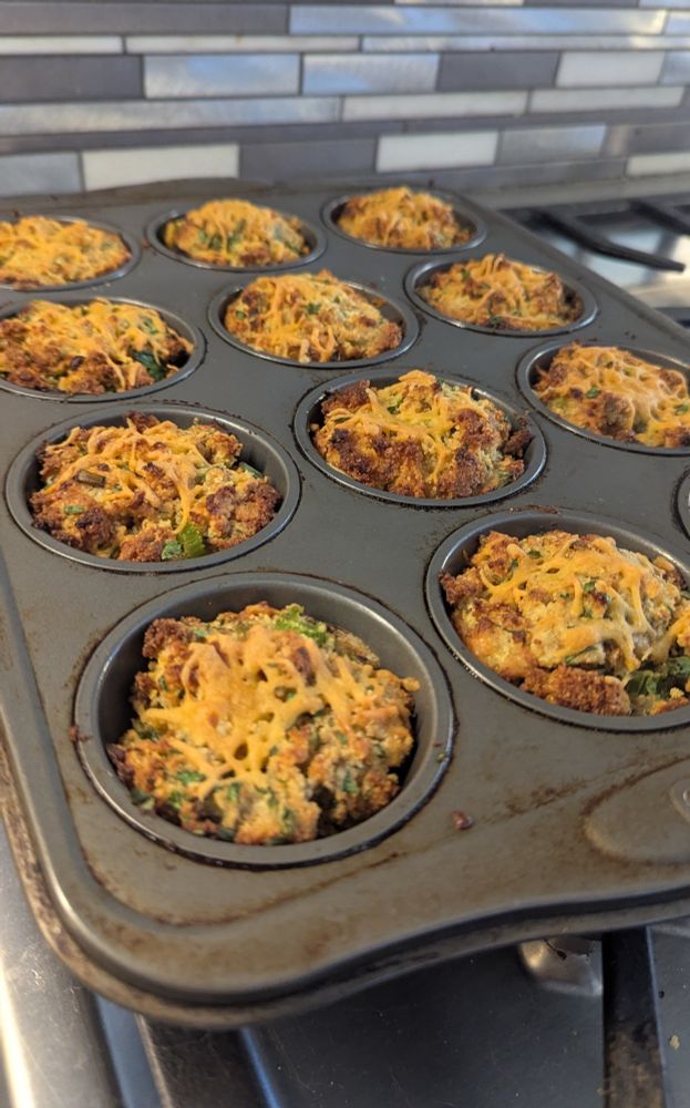 The same stuffing mix after baking in a muffin pan. The cornbread stuffing muffins are topped with more cheddar cheese, and both the cheese and cornbread stuffing are browned in the edges.