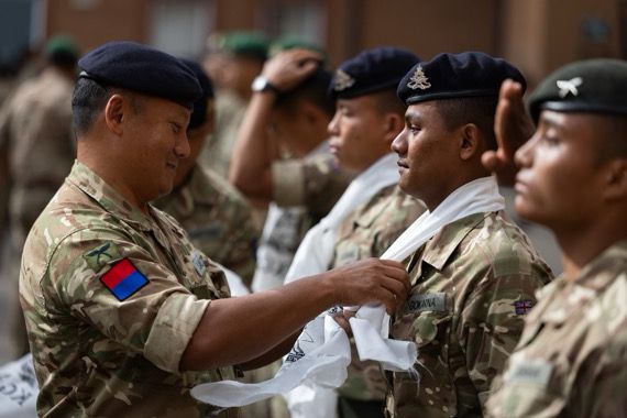 A British Army officer is tying a white scarf around the neck of a soldier.