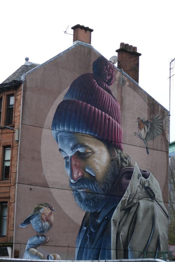 A mural of a man with a robin on his hand and a robin about to alight on his shoulder