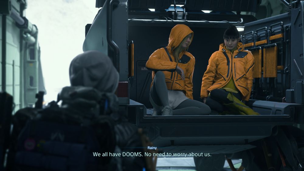Rainy and Tomorrow from Death Stranding 2 are sitting just inside the trunk of one of the large delivery trucks, aboard the Magellan. They're about to depart on a trip to acquire supplies to upgrade the fix the ship. Rainy says to Sam, "We all have DOOMS. No need to worry about us.".