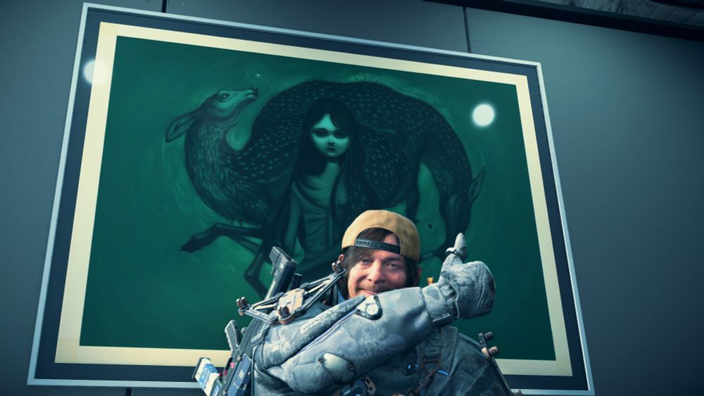 Sam standing in front of a hanging painting in the Artist's facility. It's a painting made by artist Lauren Tsai. Sam is holding up a thumbs up and smiling.