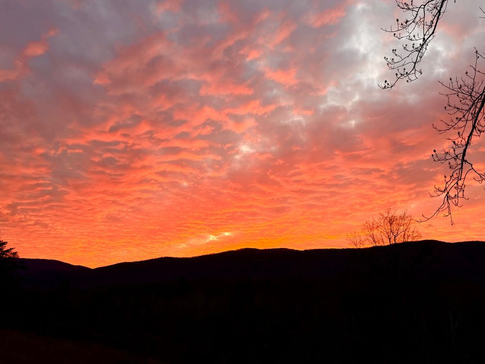 Pink and salmon sunset clouds over black low mountains 