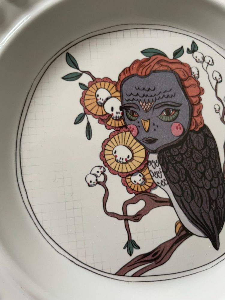 Ceramic plate with an illustration of an owl and flowers. The flowers have little skulls in the center 
