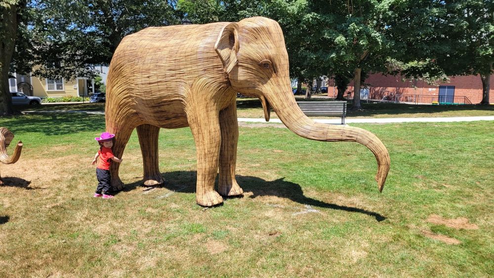 A small child hugging the leg of a large elephant statue in a park