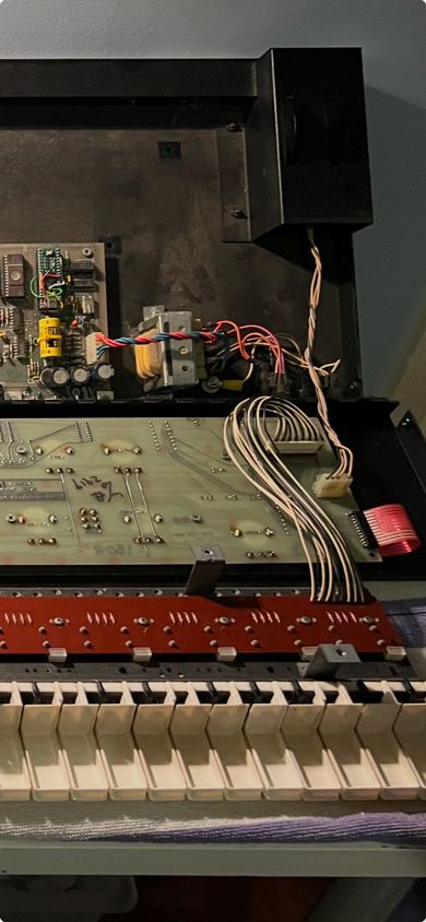 Wires, a circuit board, white piano keys. The inside of a Prophet 600 synthesizer. 