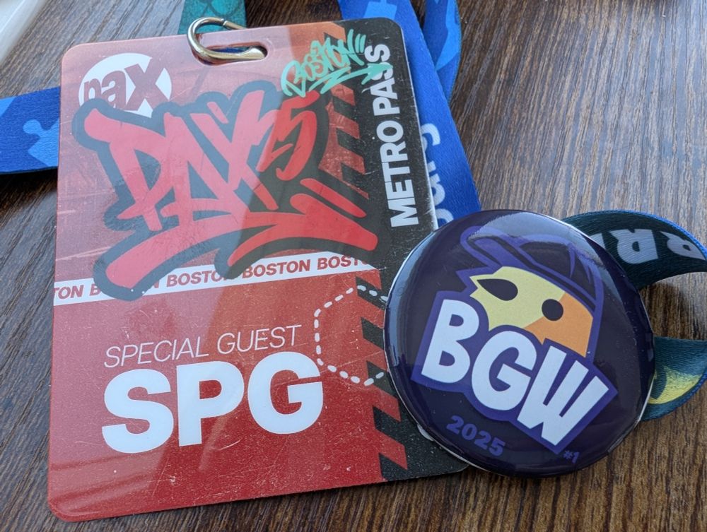A PAX '25 special guest pass and a blue pin. It features a yellow bird wearing a cap with "BGW 2025" Written below. There's a very tiny "#1" next to the letters.