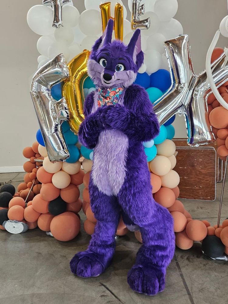 Niqnaq in fullsuit standing in front of fox colored balloons