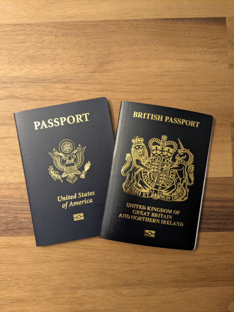 Both my US passport and British passport side by side, on a lovely wooden desk top.