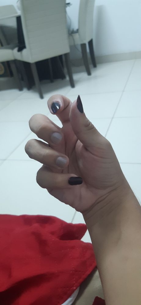 foto de mão com os dedos pra dentro, unhas pintadas e cadeiras ao fundo.