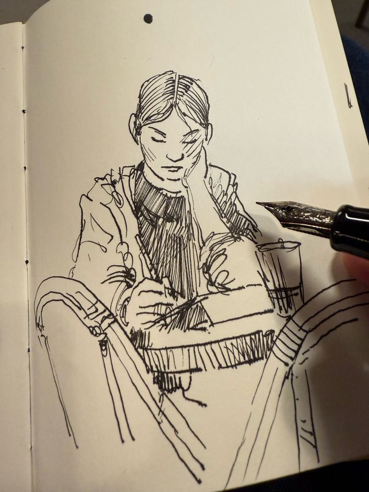 An Indian ink sketch on paper of a woman using an iPad in a coffee shop in Hong Kong. The picture depicts the process, showing part of the fountain pen. Drawing on location.