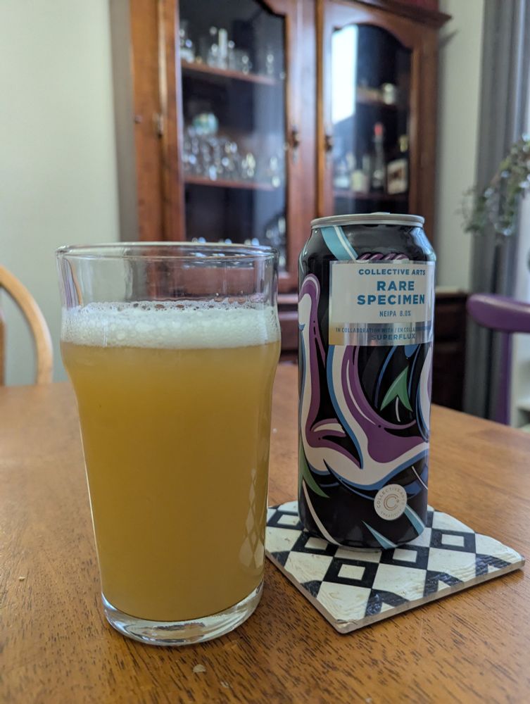 A glass of beer next to the can from which it was poured. The beer is yellow and hazy. The can says "Rare Specimen NEIPA".