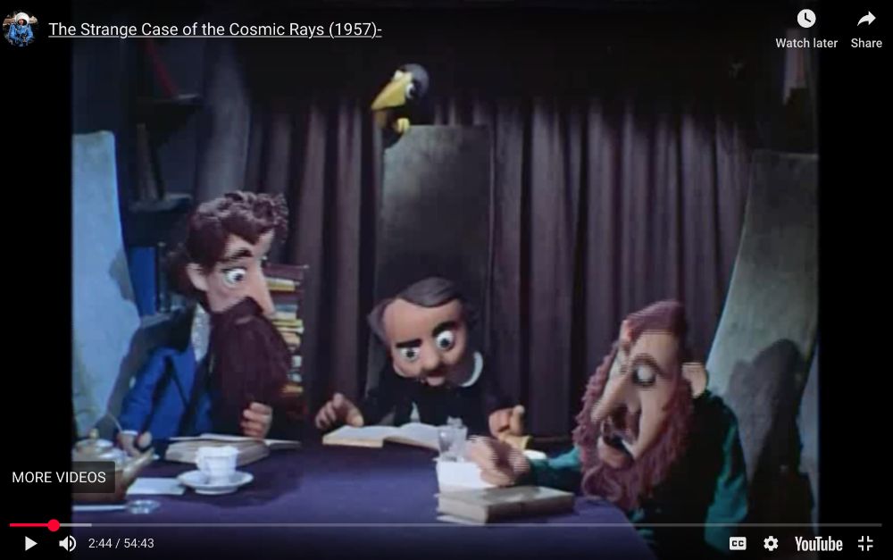 Screen shot of a 1957 film, the Strange Case of the Cosmic Rays, featuring puppets of Dickens, Poe and Dostoevsky, sat around a table looking at books, with Poe’s raven on the back of his chair. 