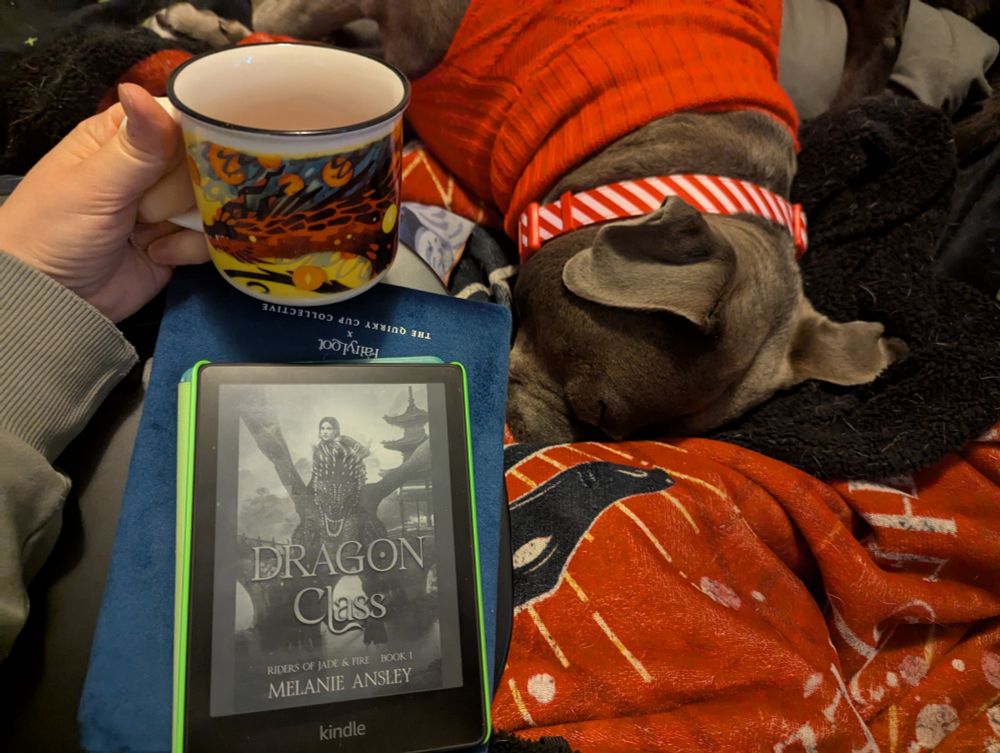 A mug of tea in my left hand, my Kindle on my lap displaying the cover of "Dragon Class" by Melanie Ansley, and my blue pitbull mix dog names Luna snuggled nearby.