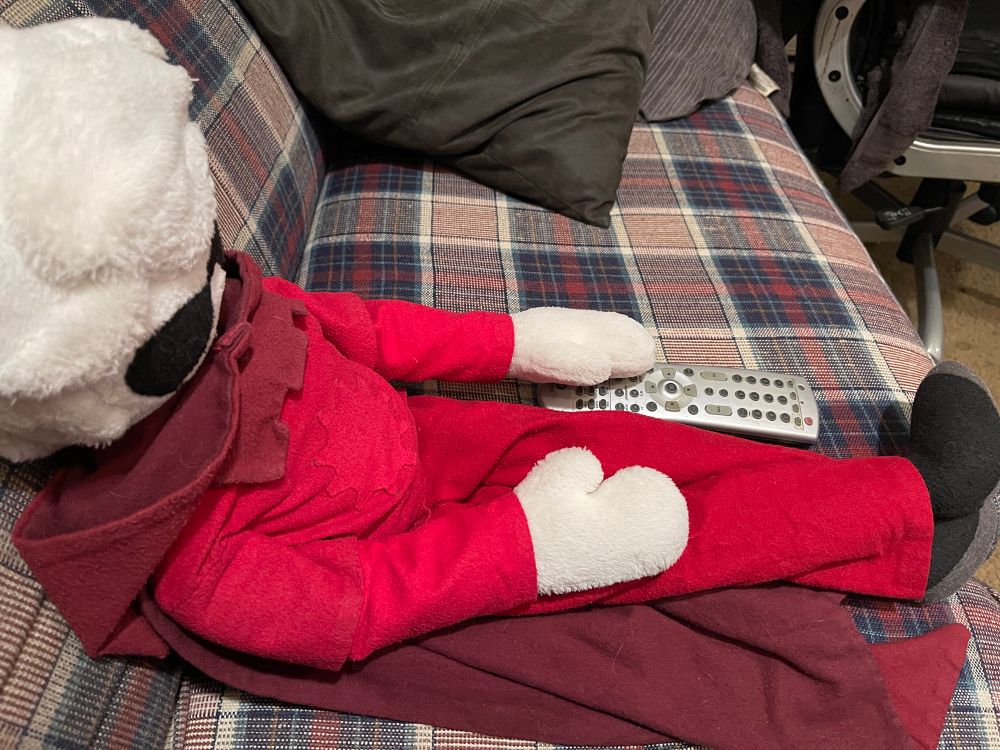 Plush Dave Strider chilling on the couch next to the viewer, one hand resting gently on the TV remote. 