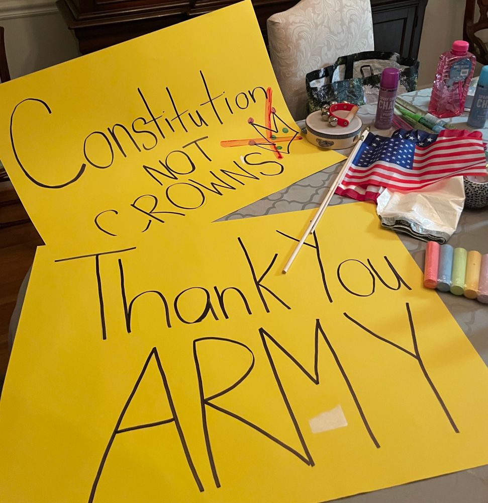 Yellow posters with writing “Thank you ARMY” and “Constitution, not Crowns” with assorted other protest gear like American flags and sidewalk chalk.