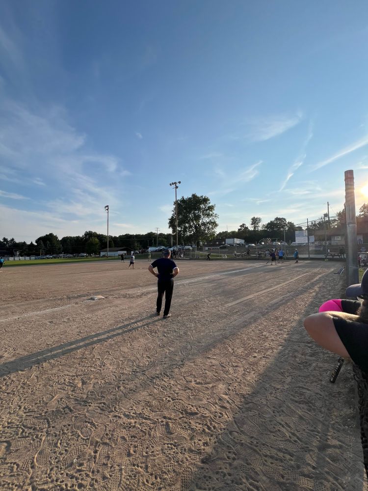 A picture of a baseball field taken from the 3rd base side facing home. Long shadows are over the field from the sun low behind home