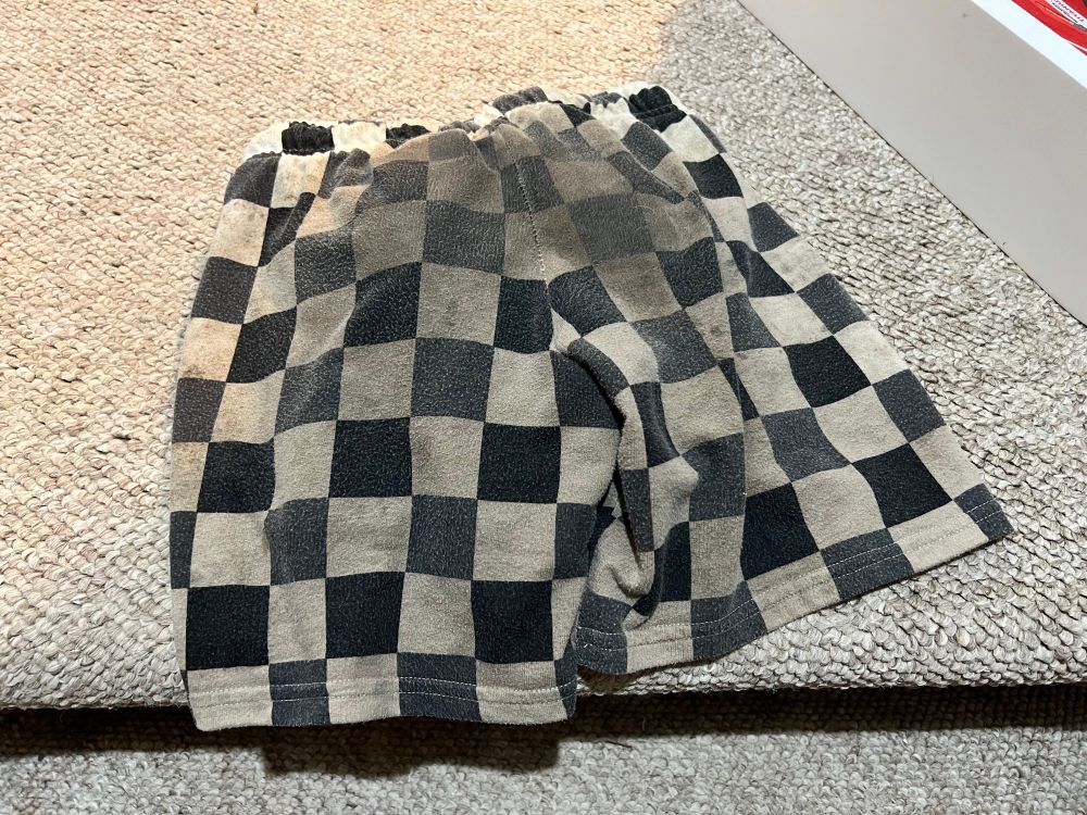 Checkered kids shorts on a carpeted floor. The shorts have a black & white checkerboard pattern but there really is no white left. Everything is gray, wet, and muddy with even darker gray in the middle.
