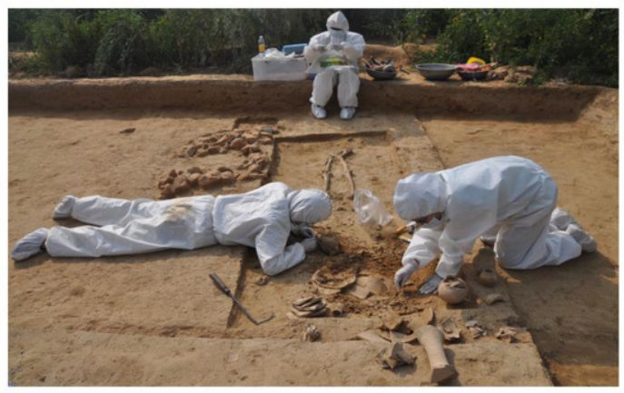 Three researchers at an acient dig site, completely covered by hazmat suits, gloves, booties, hoods and masks.
