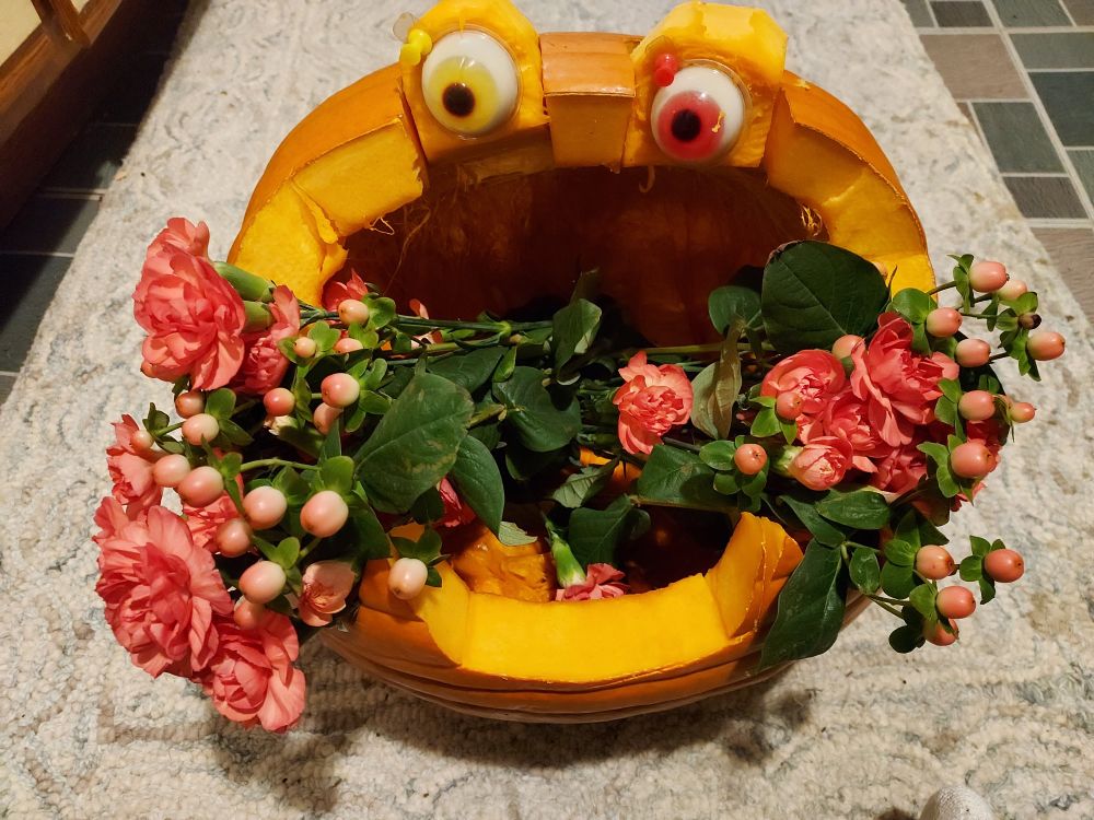 Googly-eyed jack-o-lantern with carnations in its mouth.