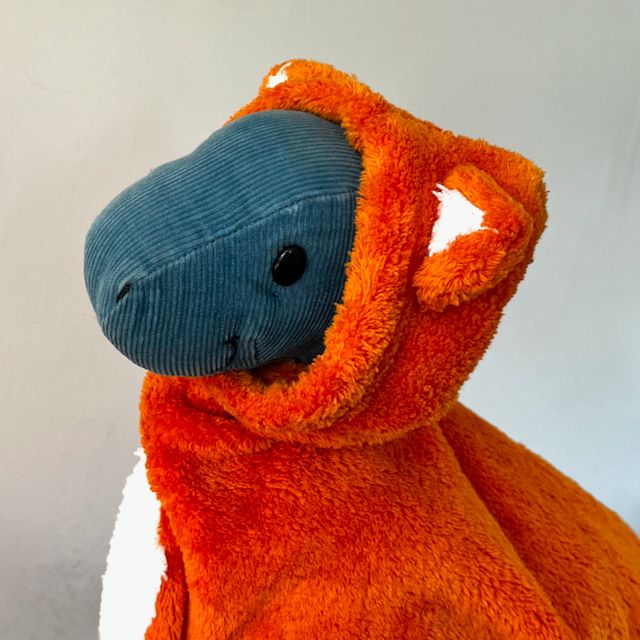 Dinosaur plush toy wearing a orange and white hoodie with pointed ears.
