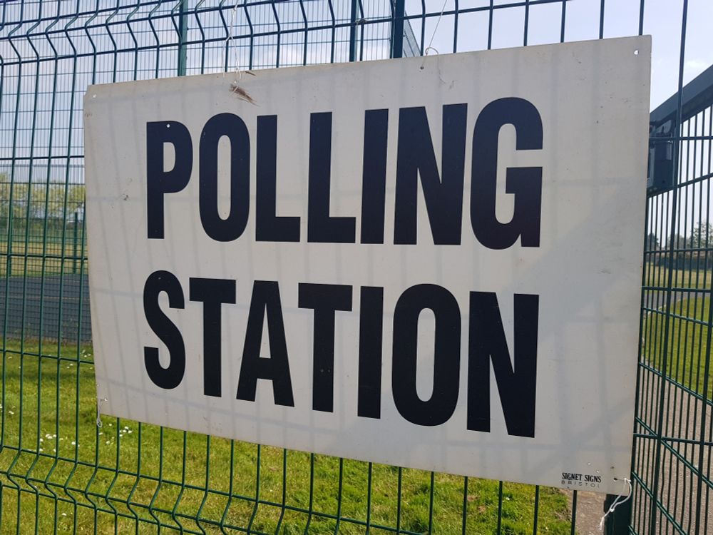 Polling station sign attached to a fence with field in the background.