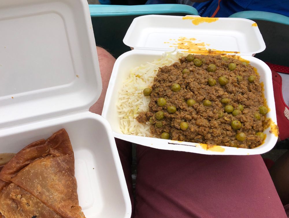 A takeaway box of lamb curry and rice with a samosa. 
