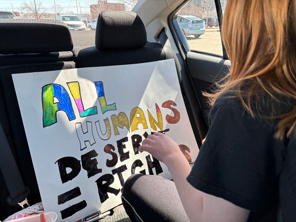 Child creating protest sign “All humans deserve = rights”