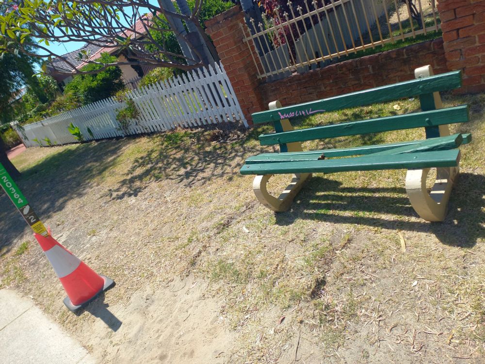 Transperth bus stop 20364 along the 514 bus route to Cockburn, with a road cone wrapped around the signpost and one of the three wooden beams making up the seat portion of the bench snapped in half