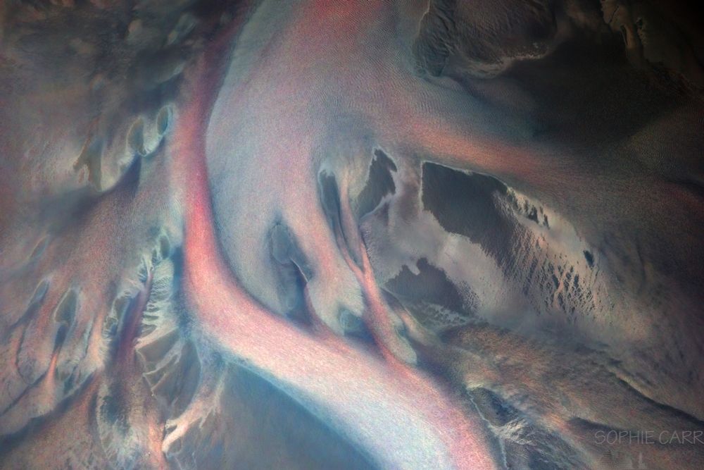 An abstract network of river braids photographed from a drone. The colours have been inverted (opposite hue on the colour wheel), resulting in some weird reds where the rivers are turquoise.