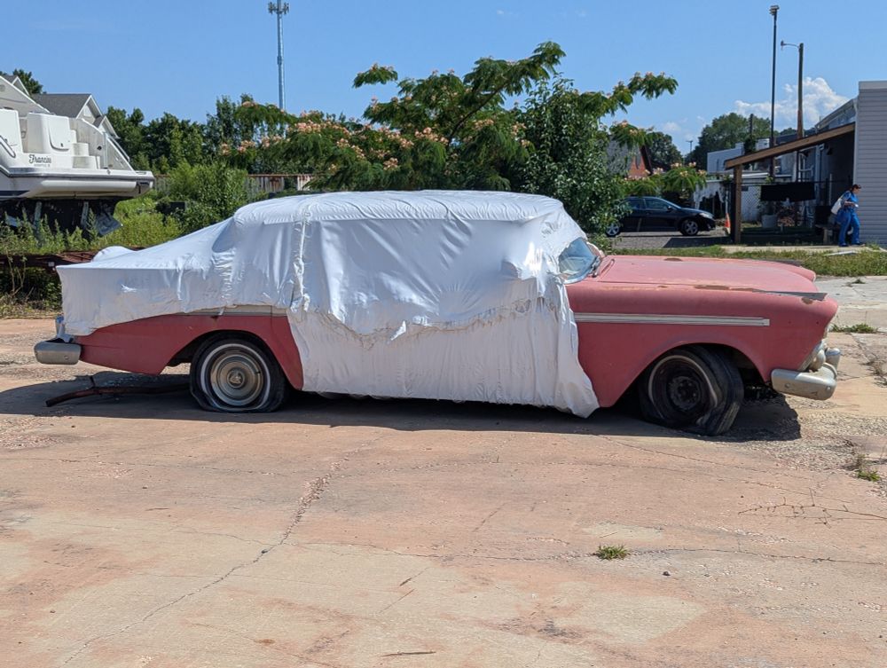 Old red car half under sheet