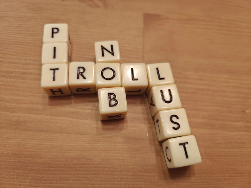 Dice with letters on them, arranged in a crossword style fashion. The words intersect and spell troll, lust, nob, pit