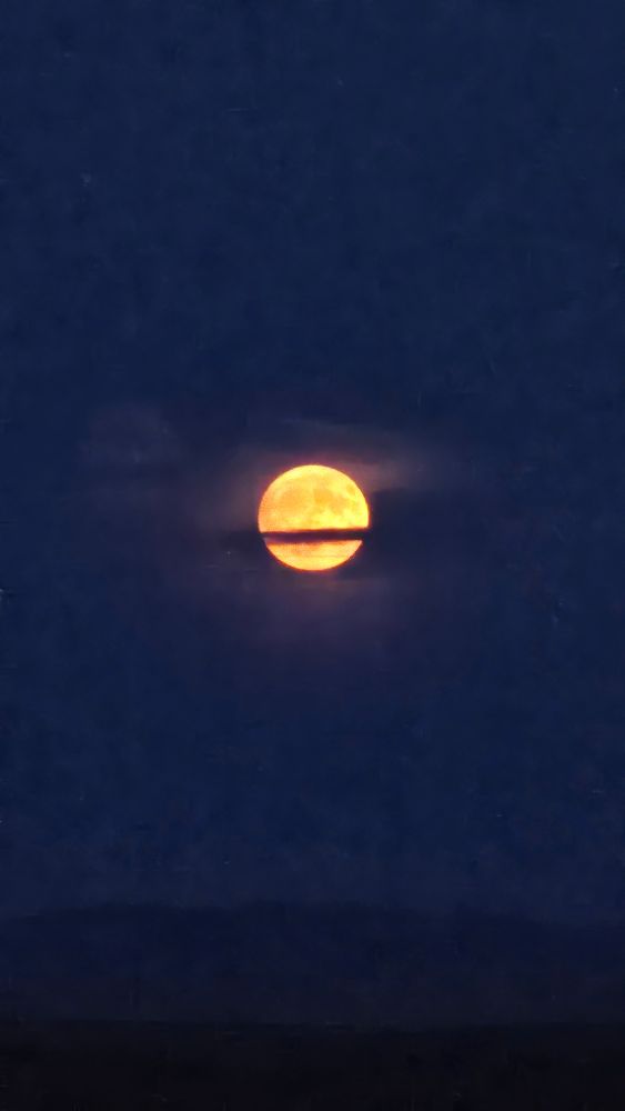 A deep red full moon with thin trails of cloud across it
