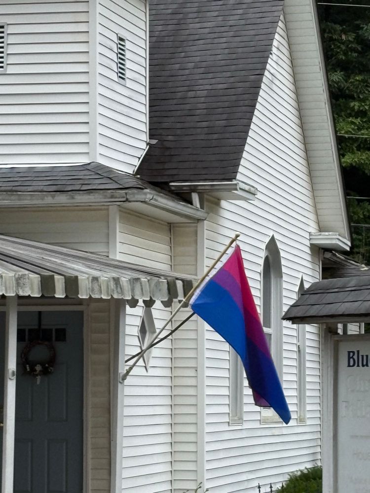 A rural church proudly displaying a bi-pride flag right by the main entrance 
